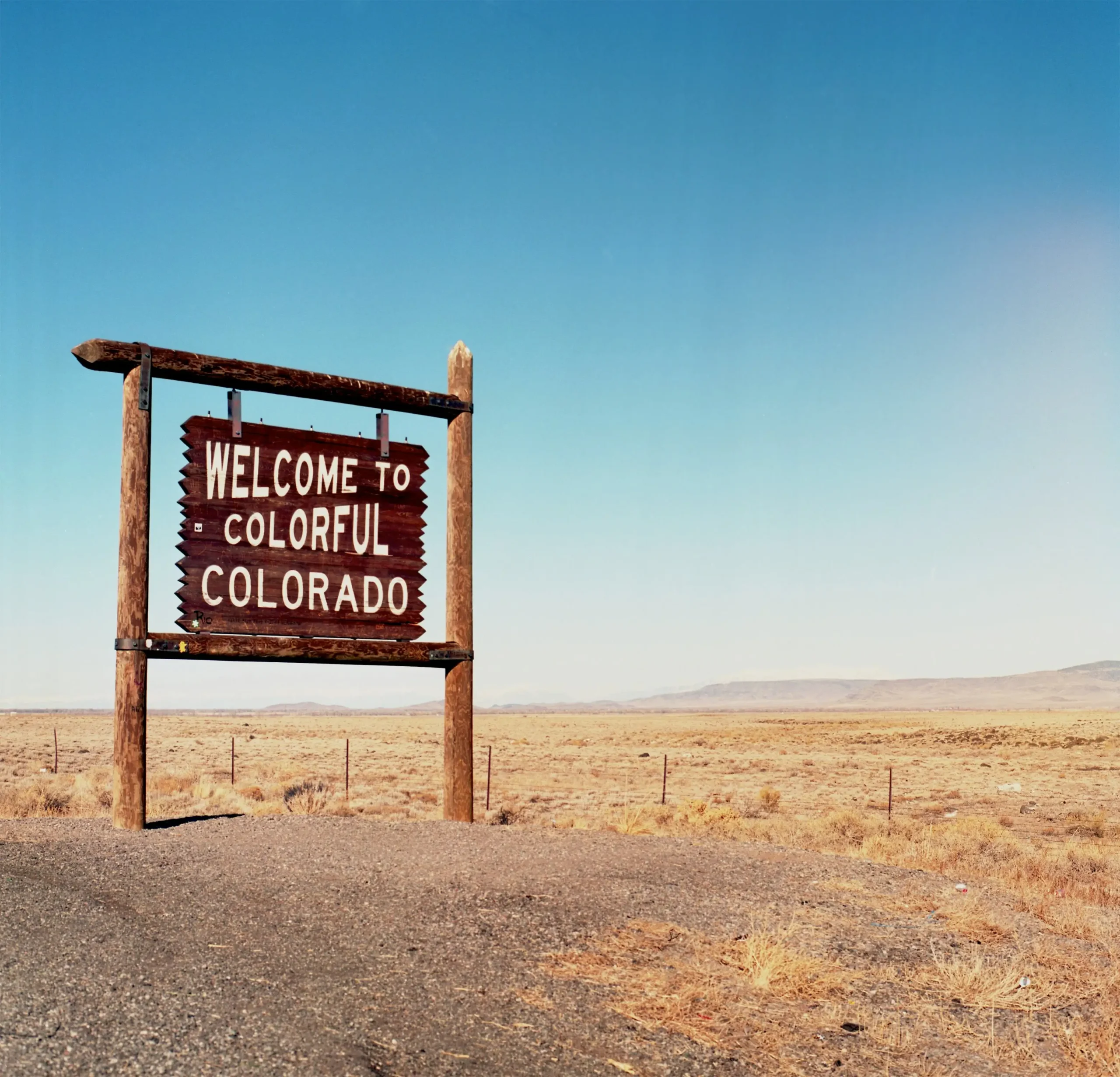A wooden sign reading "Welcome to Colorful Colorado" in front of a field of dry grasses.